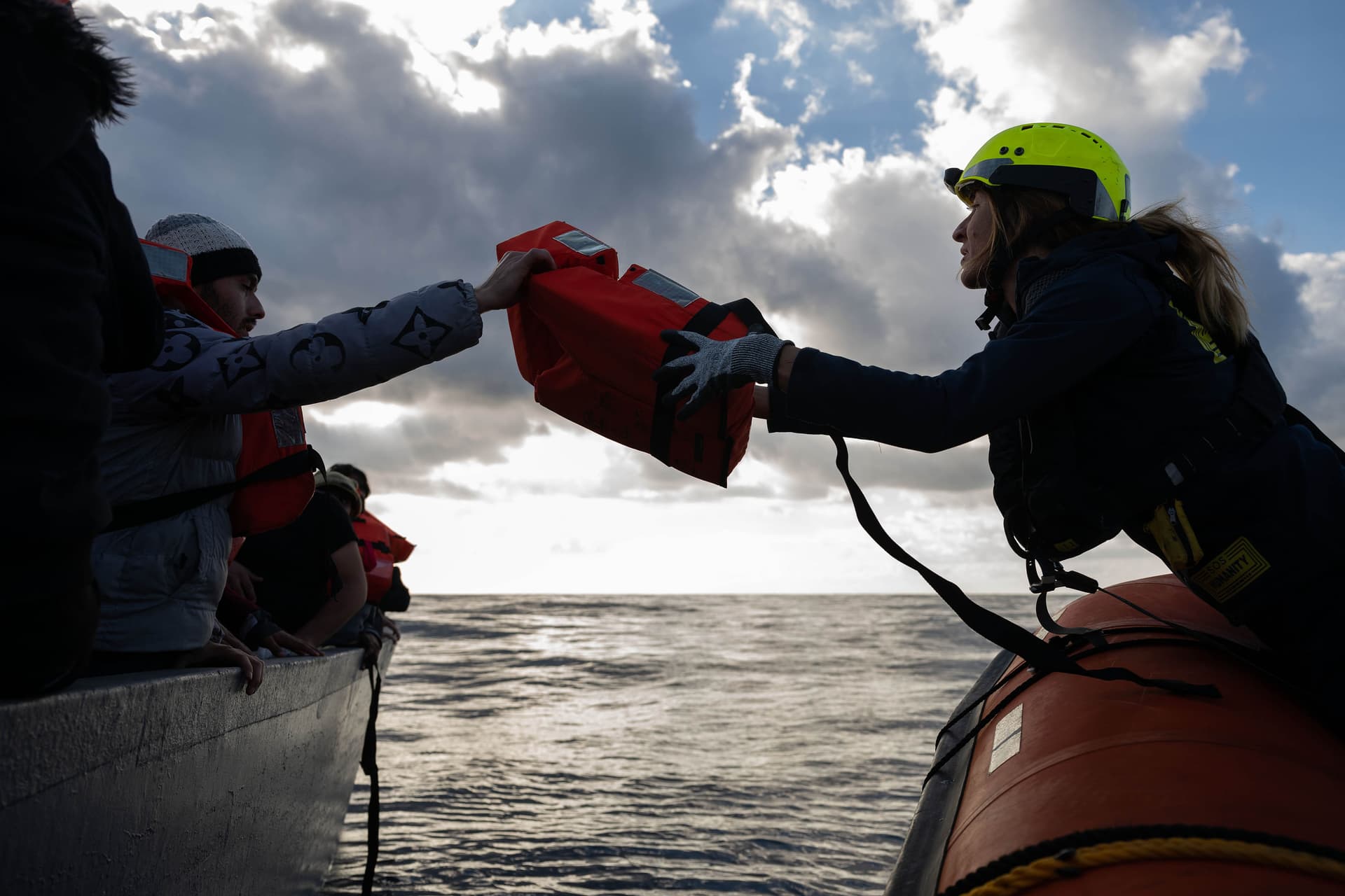 Einem flüchtenden Menschen auf einem Boot wird eine Rettungsweste übergeben